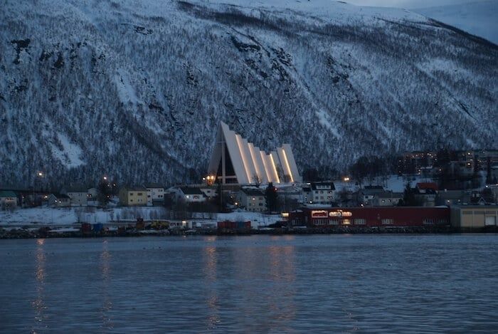 Vinterkledd Tromsø med Ishavskatedralen ved fjorden i skumringen