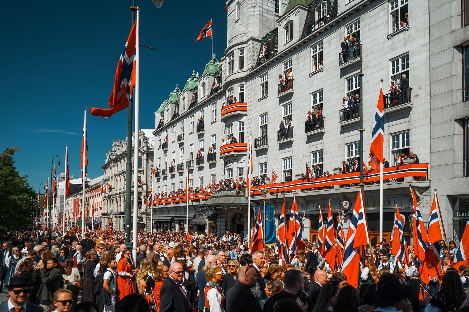 Folkemengde med norske flagg utenfor pyntede bygninger