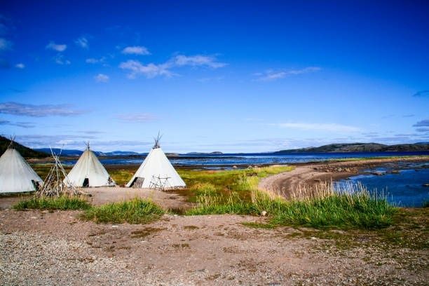 Tre lavvoer ved en fjord i et åpent, nordnorsk kystlandskap