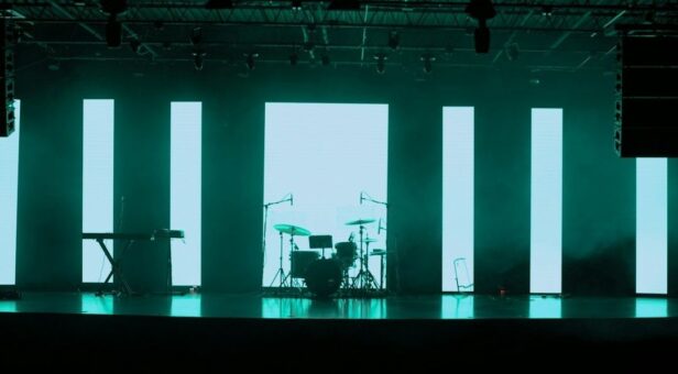 Belyst festivalscene med trommesett, keyboard og høye LED-paneler
