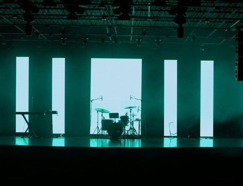 Belyst festivalscene med trommesett, keyboard og høye LED-paneler